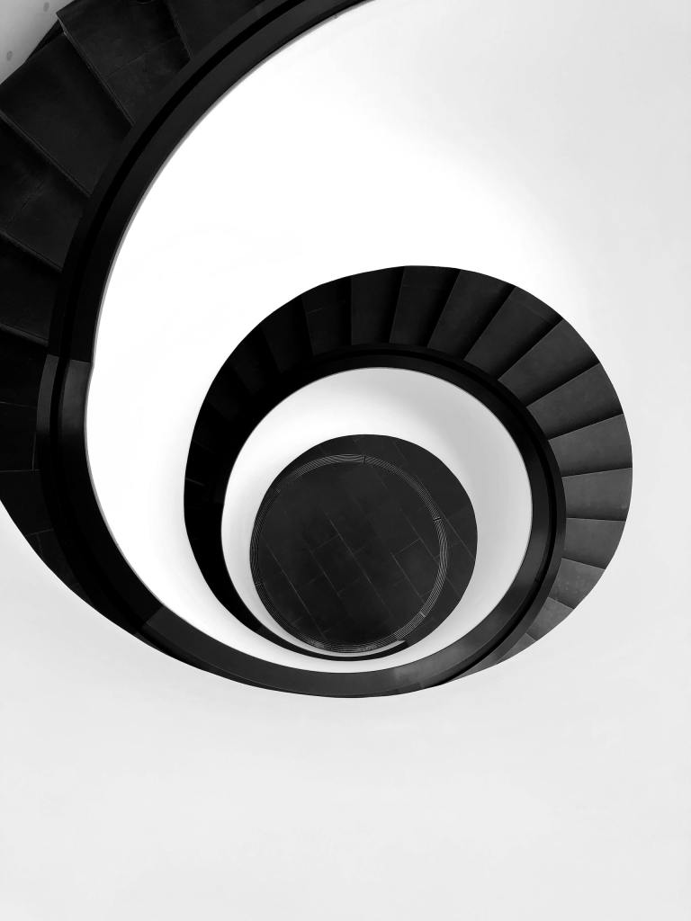 Bird view of black ladders going down while creating a spiral pattern on a white background