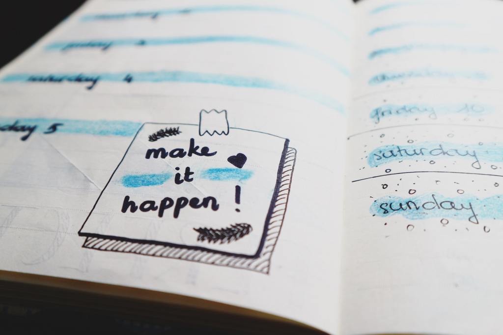 A notebook with a post note of a "make it happen!" text